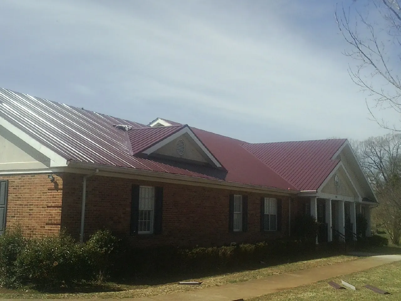 Red metal roof with gabled entries on a long brick building, from a Hail Damage Roof Repair job in Manasquan