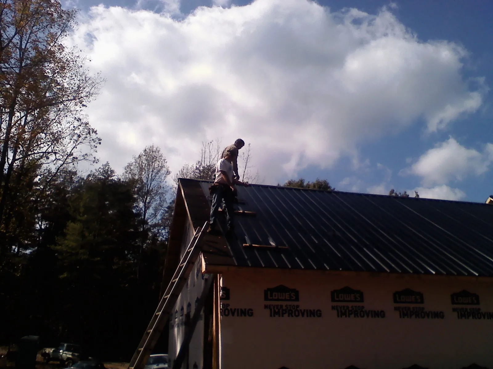 Roofer fastening dark metal panels high against a cloudy sky, from a Roof Inspection job in Manasquan