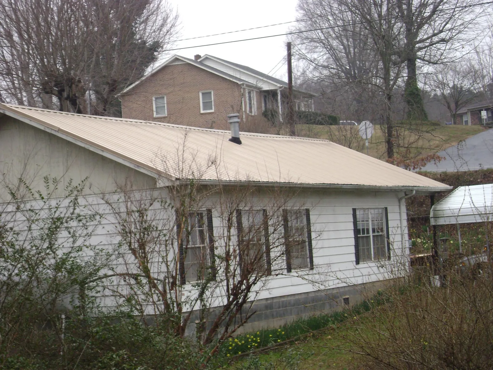 Tan metal roof on a white sided house set into a hillside — Commercial Roofing by Roofing Brothers in Manasquan